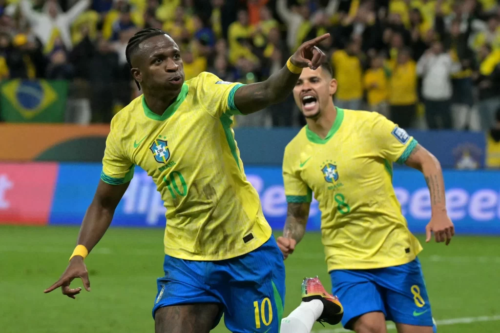 Vinícius Júnior comemora gol pelo Brasil nas Eliminatórias da Copa do Mundo 2026 com Bruno Guimarães ao fundo, em partida que garantiu vaga antecipada à Seleção Brasileira.
