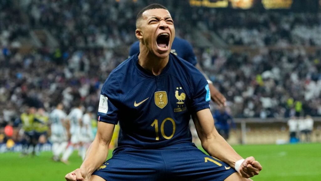 Kylian Mbappé comemorando gol pela França na Copa do Mundo 2022, destacando o artilheiro da competição com braços abertos.