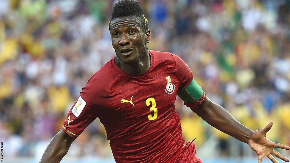 Asamoah Gyan, capitão da seleção de Gana, vestindo a icônica camisa 3 branca durante partida da Copa do Mundo de 2014.